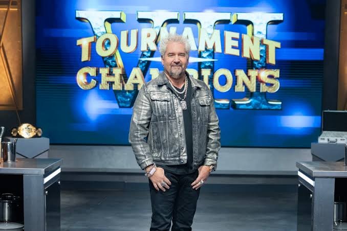 Guy Fieri hosting Tournament of Champions Season 7 cooking competition with chefs competing in a kitchen arena.